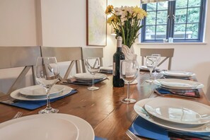 A dining table set with plates, glasses, and a bottle of wine, with a vase of flowers in the center. - Corner Cottage, Thorpeness (Leiston)