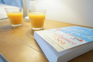 Una mesa de madera con dos vasos de jugo de naranja y un libro titulado 'Summer at Sea'.