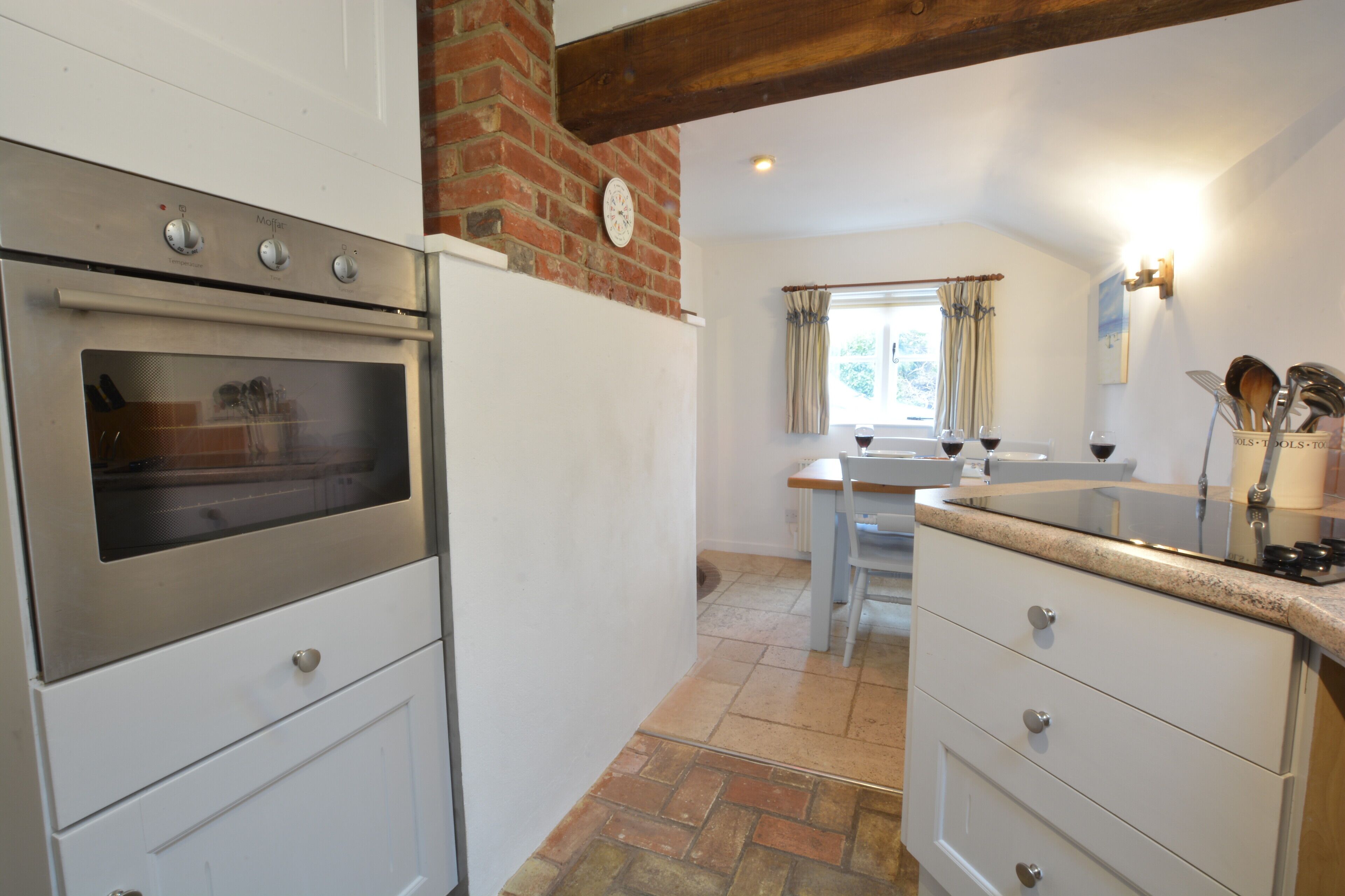 A kitchen with a built-in oven, white cabinets, a brick wall, and a window with curtains.
