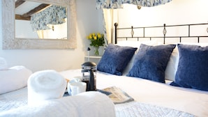 Una cama bien hecha con ropa de cama azul y blanca, una cafetera y un periódico sobre la mesita de noche.