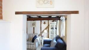 Una sala acogedora con un sofá azul, un sillón a rayas y techo con vigas de madera.