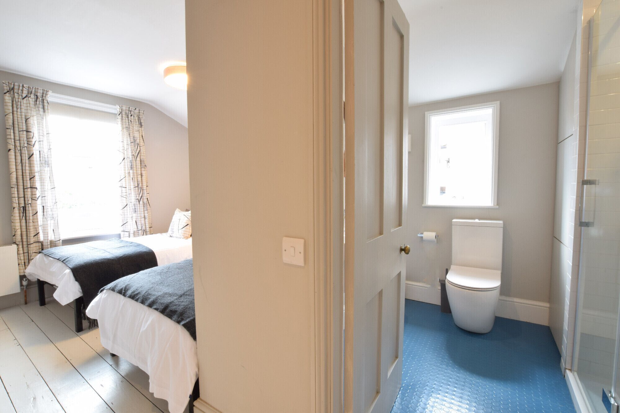 A bedroom with two beds, a bathroom with a toilet and a shower, and a hallway with a door.