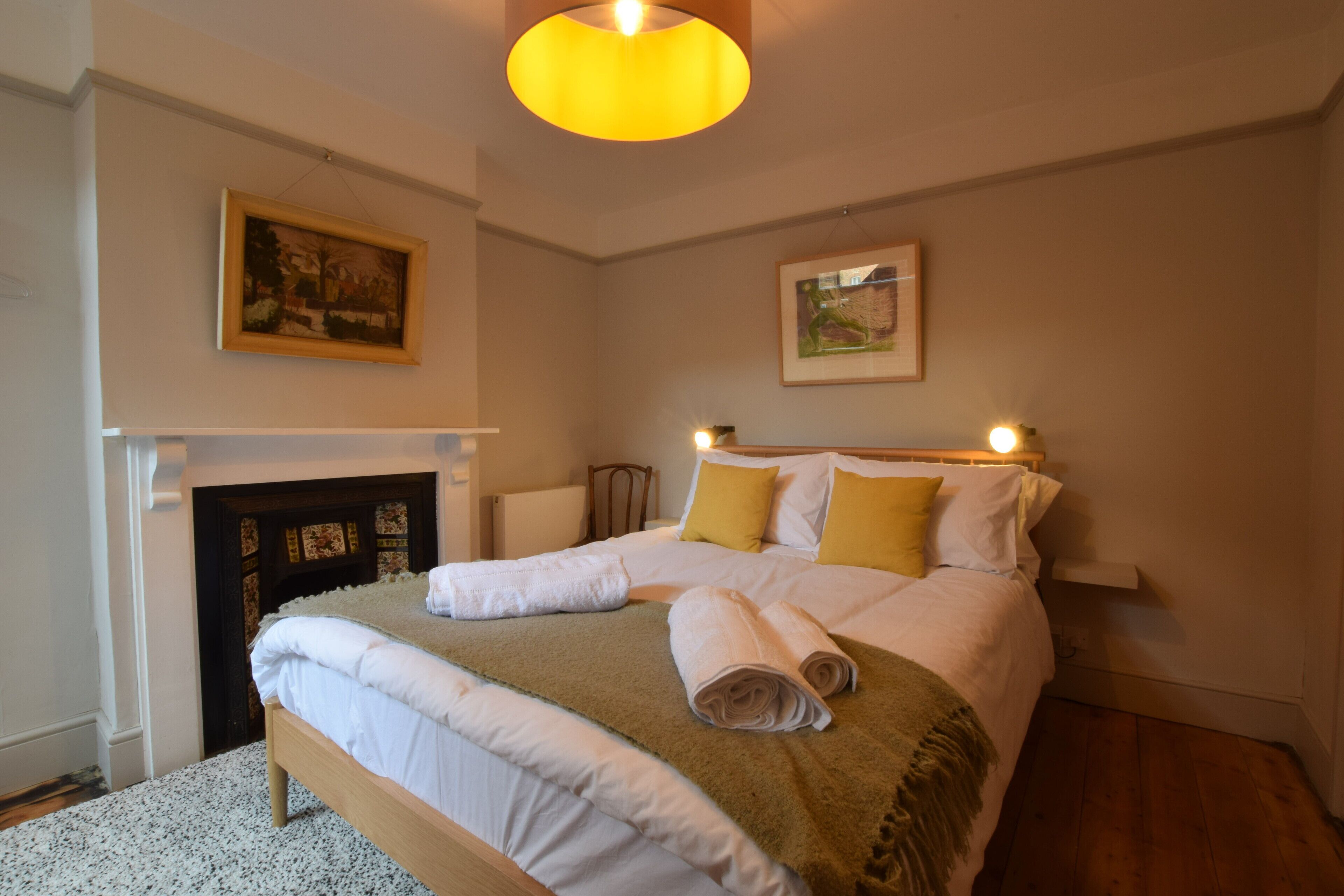A neatly made bed with white linens and a brown throw, a wooden headboard, and a painting above it.