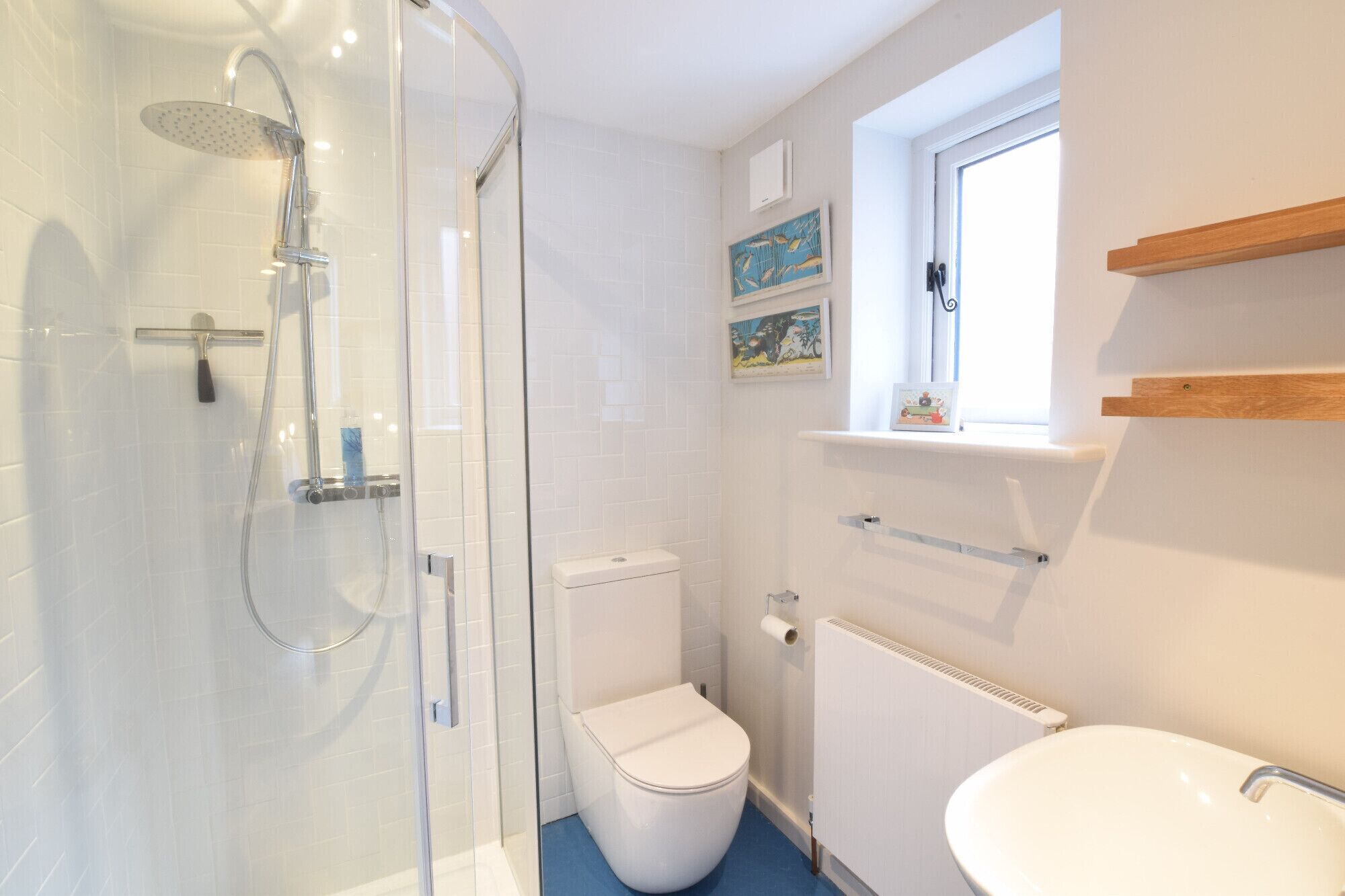 A bathroom with a glass-enclosed shower, a white toilet, a white sink, and a window above the sink.