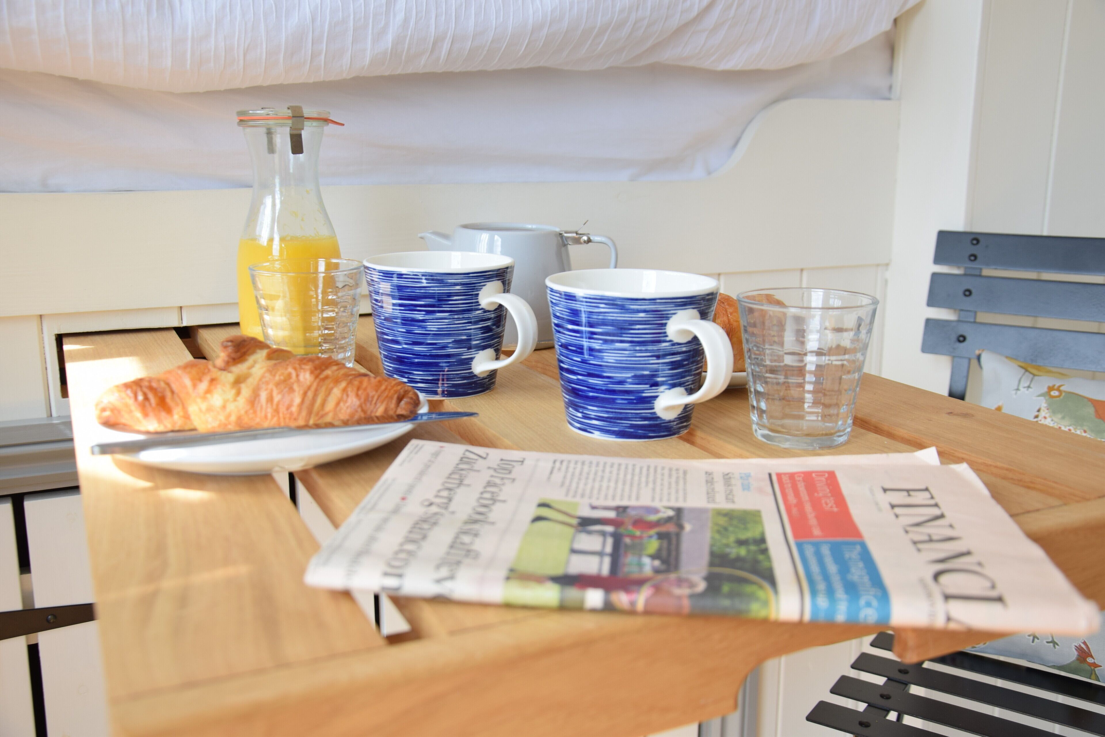 Une table de petit-déjeuner avec un croissant, un journal et une bouteille de jus d’orange.