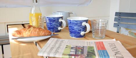Une table de petit-déjeuner avec un croissant, un journal et une bouteille de jus d’orange.