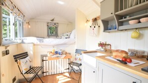 A compact kitchen with a wooden countertop, a drying rack, and a small dining area with a bench.