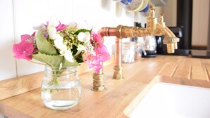 A kitchen counter with a clear glass vase containing pink and white flowers, a copper faucet, and a white sink.