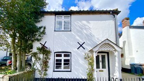 A white building with two windows and a door, surrounded by a black metal fence. - Satis Cottage, Westleton (Saxmundham)