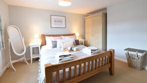 A neatly arranged bedroom with a wooden bed, bedside tables, a hanging lamp, a wardrobe, and a trash bin. - Satis Cottage, Westleton (Saxmundham)