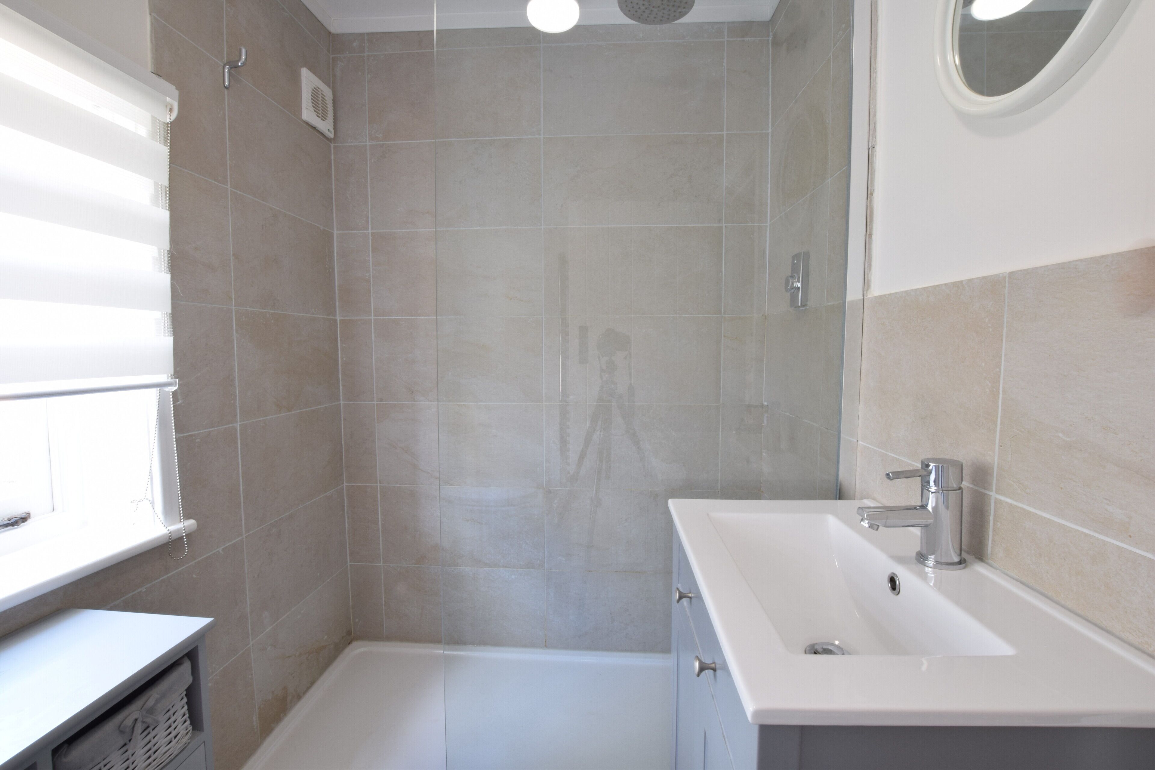 A bathroom with a shower, sink, and a window with blinds.