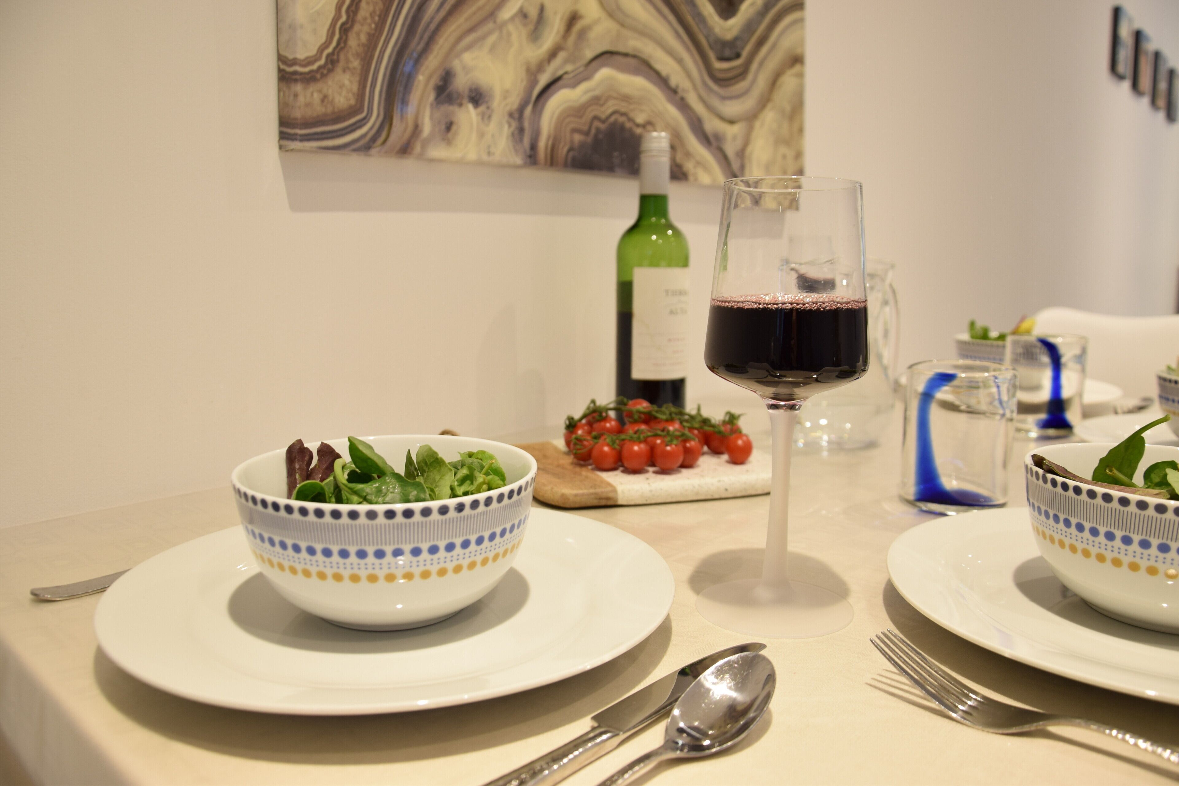 A dining table with a salad bowl, a wine glass, and a bottle of wine.