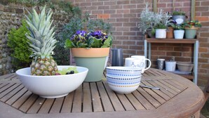 Una mesa de madera con un frutero, una planta en maceta y una taza.