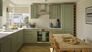 Une cuisine moderne avec des meubles de couleur verte, une table à manger en bois et une vue sur l’extérieur.