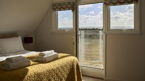 Une chambre avec un lit, deux fenêtres et vue sur la plage.