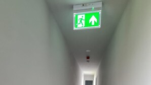 A narrow, carpeted hallway with white walls and a green emergency exit sign. - Luxury Apartment - Free Wi-fi & Parking NO Deposit (Coventry)