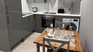 A compact kitchen with grey cabinets, a built-in oven, a microwave, and a washing machine. - Luxury Apartment - Free Wi-fi & Parking NO Deposit (Coventry)