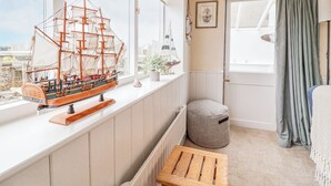 A room with a large window, a wooden bench, a small ottoman, and a model ship on the windowsill.