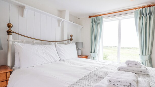 A neatly made bed with white linens, a wooden headboard, and a patterned throw. There are two bedside tables with lamps, and a window with curtains.