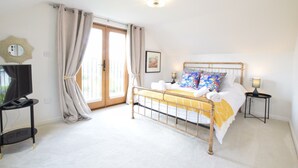 A bedroom with a bed, a television, a bedside table, and a window with curtains. - Skelder, Parham (Woodbridge)