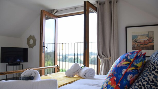 A hotel room with a bed, a TV, a balcony with a view, and a painting on the wall. - Skelder, Parham (Woodbridge)