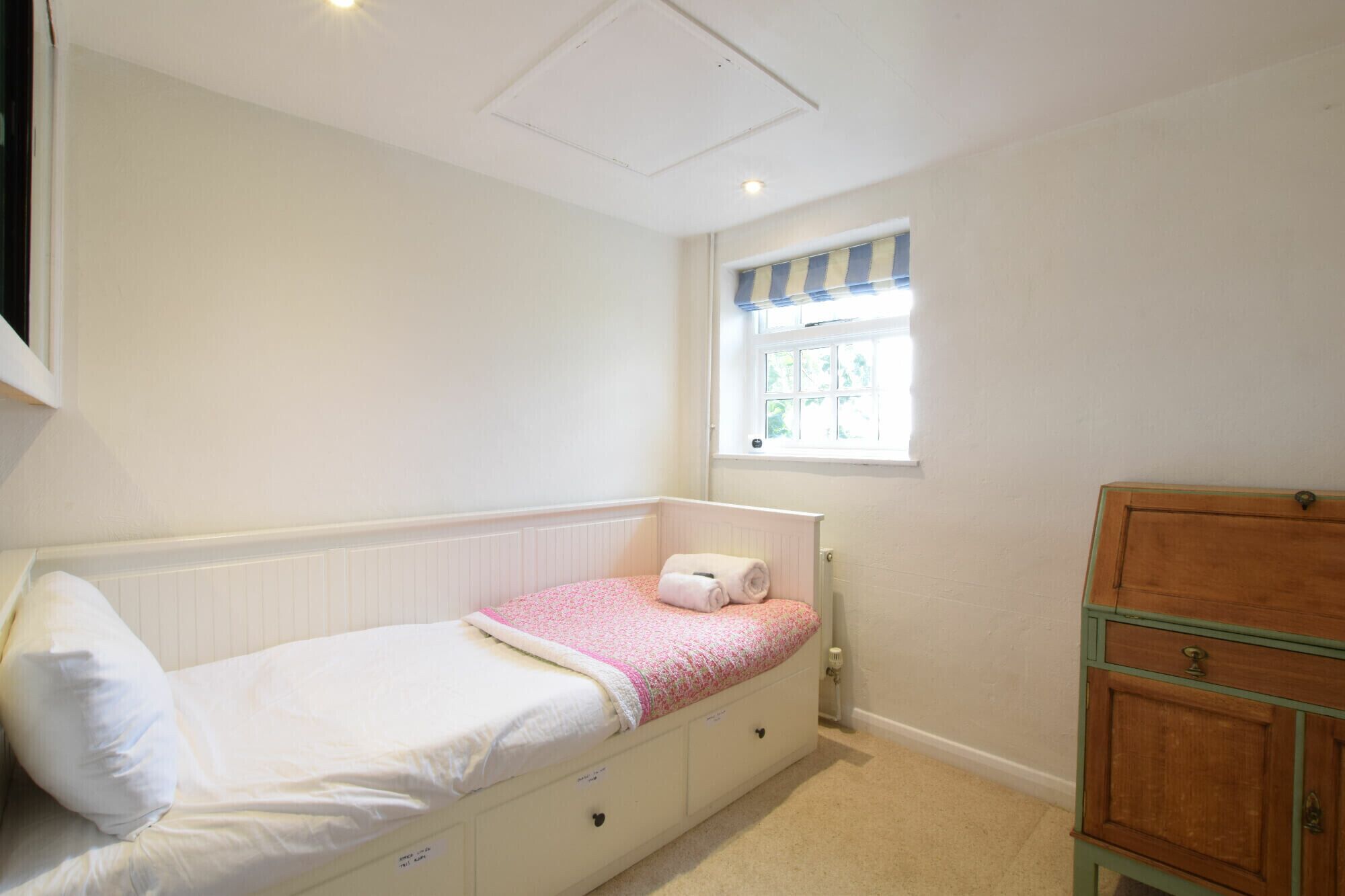 A small, single-bed room with a window, a radiator, and a wooden cabinet.