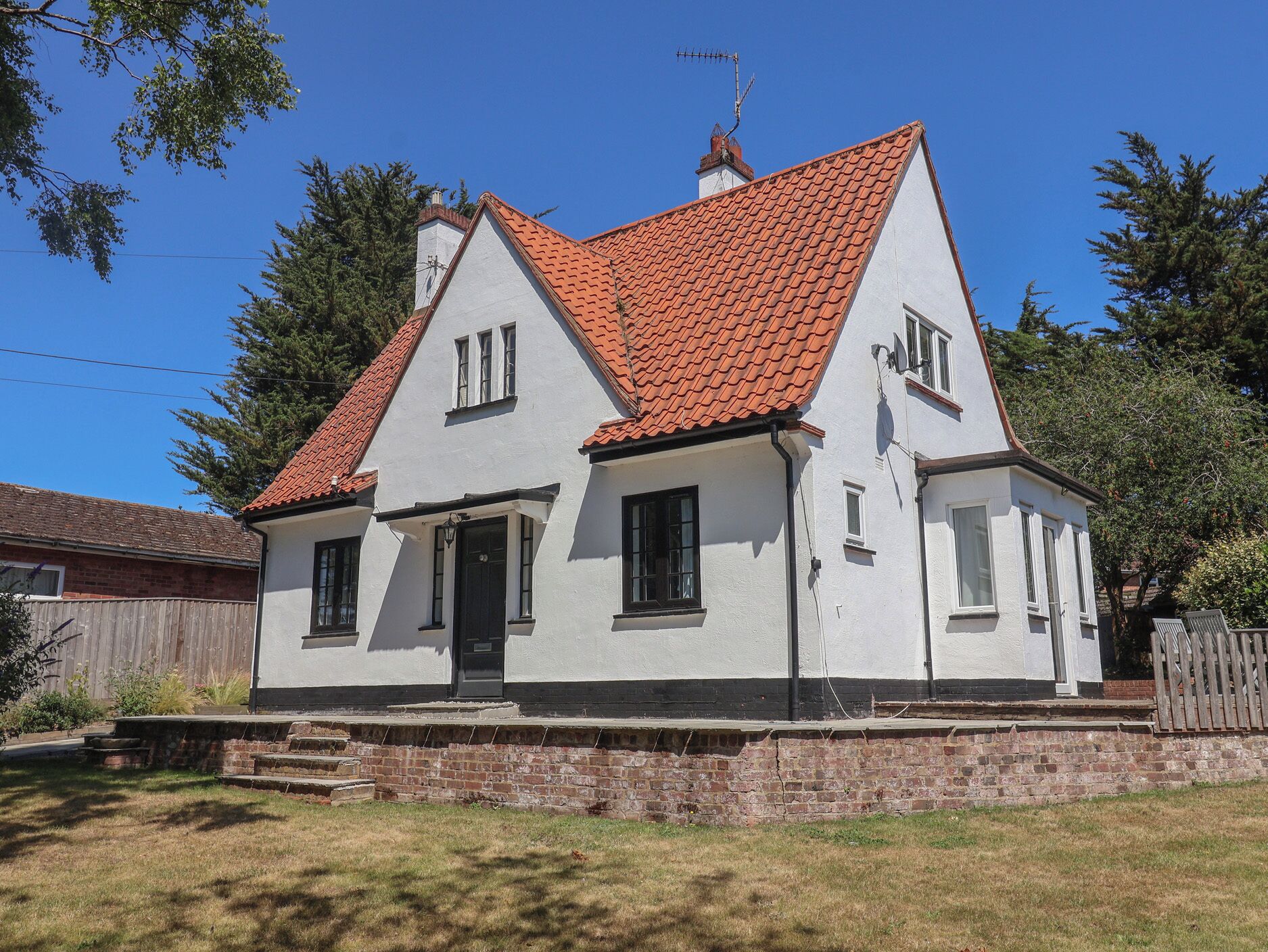A two-story house with a red-tiled roof, white exterior walls, and a brick foundation.
