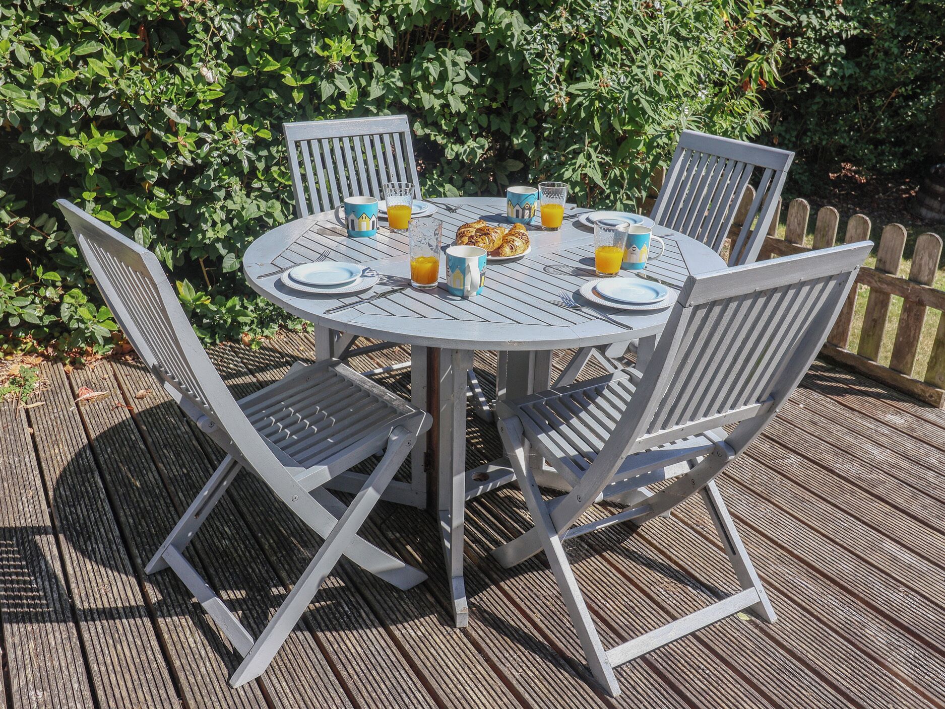 A round outdoor table with four chairs, set on a wooden deck.
