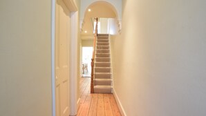 A narrow hallway with wooden flooring and a carpeted staircase. - 14 Dunwich Road, Southwold (Reydon)