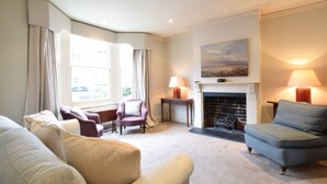 A living room with a fireplace, a sofa, a chair, and a lamp. - 14 Dunwich Road, Southwold (Reydon)
