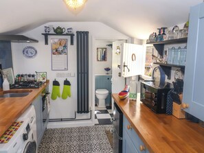 Una cocina compacta con estufa a gas, horno y microondas. Se observan guantes de horno colgados, un refrigerador y un lavamanos. La cocina tiene un piso con diseño y una ventana con vistas al exterior.