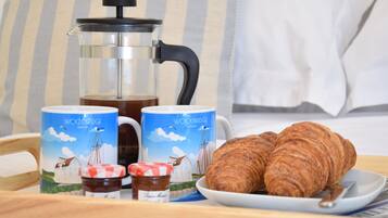A breakfast setup with a French press, two mugs, a jar of jam, and two croissants on a tray.
