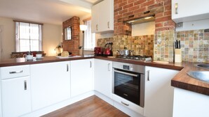 A modern kitchen with white cabinets, a brick accent wall, a Bosch oven, and a wooden countertop.