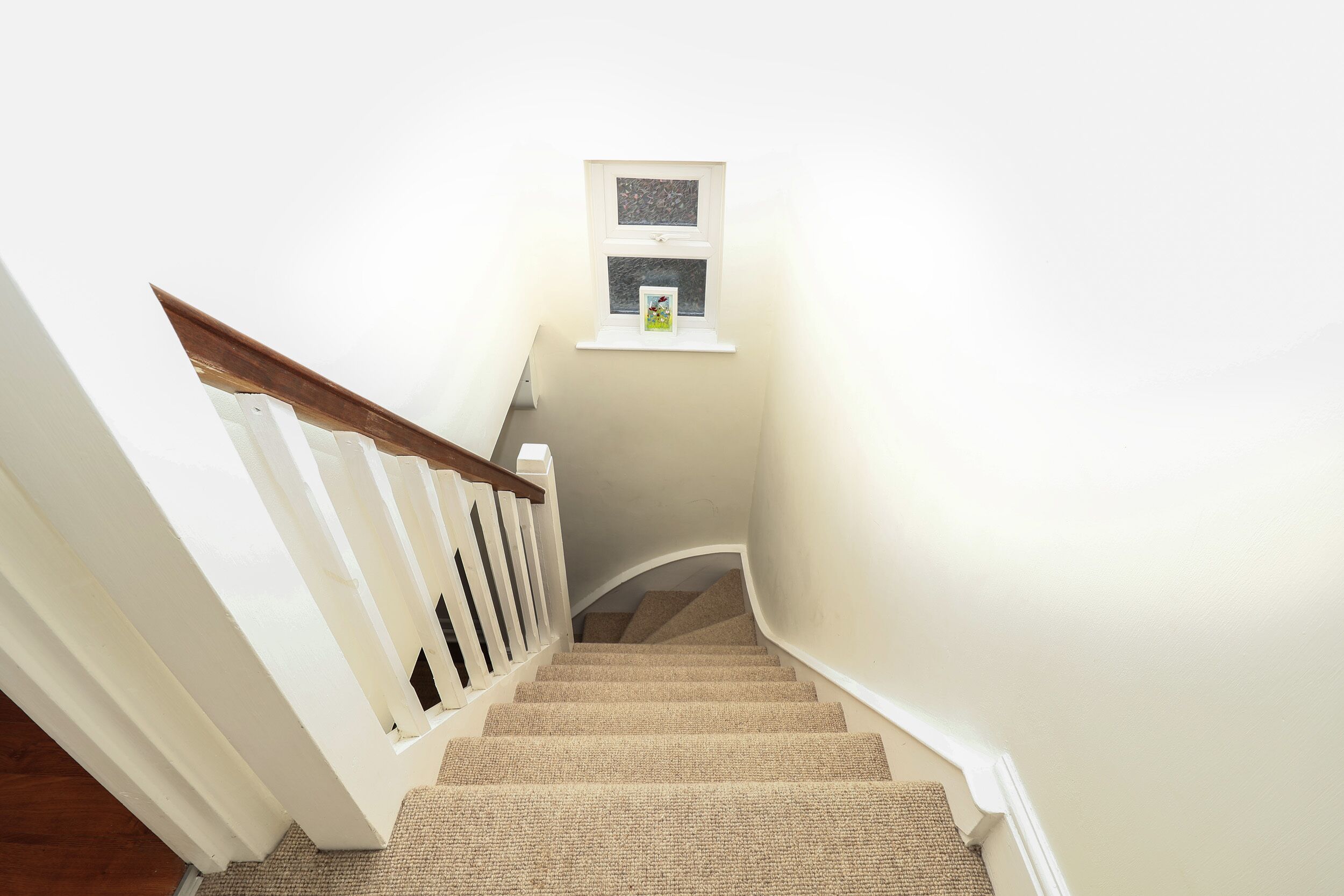 A staircase with a white railing and beige carpet leading to a landing with a small window.