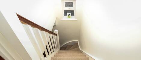 A staircase with a white railing and beige carpet leading to a landing with a small window.