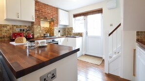 A kitchen with a wooden countertop, white cabinets, a brick backsplash, and a window with blinds.