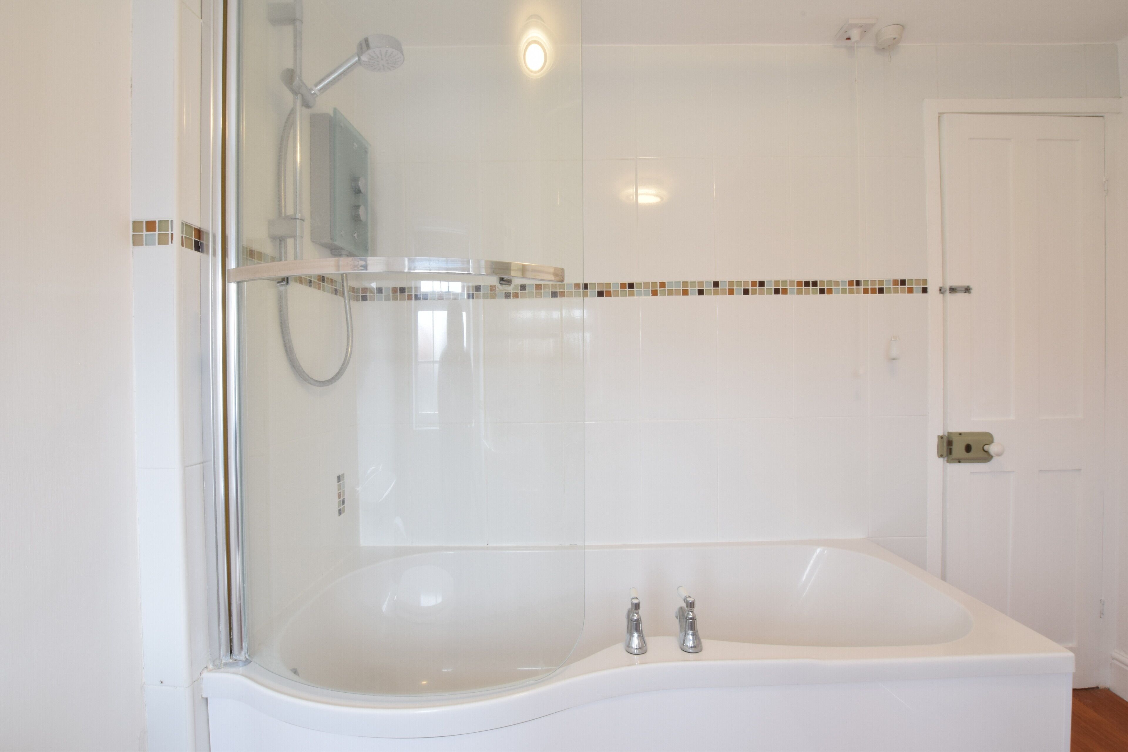 Un baño con ducha de vidrio, una bañera blanca y un muro de azulejos con detalles decorativos.