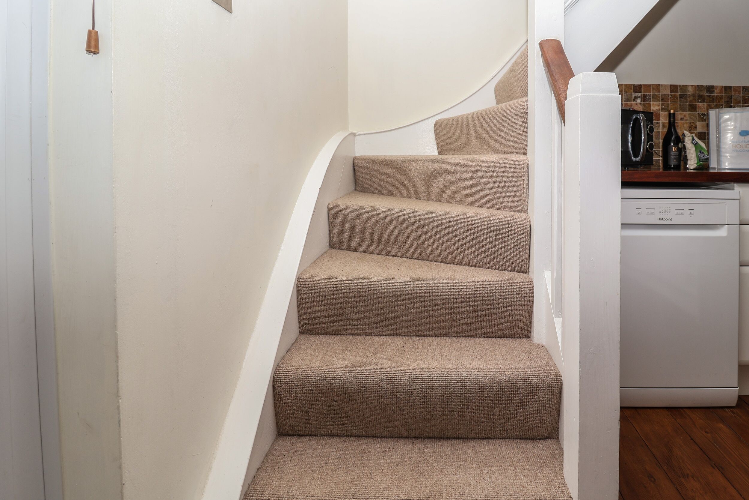 A staircase with beige carpeted steps, a wooden handrail, and a white wall.