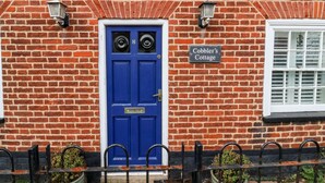 A red brick building with a blue door, a sign reading "Cobbler's Cottage," and a window with white shutters. - Cobblers Cottage, Southwold (Reydon)