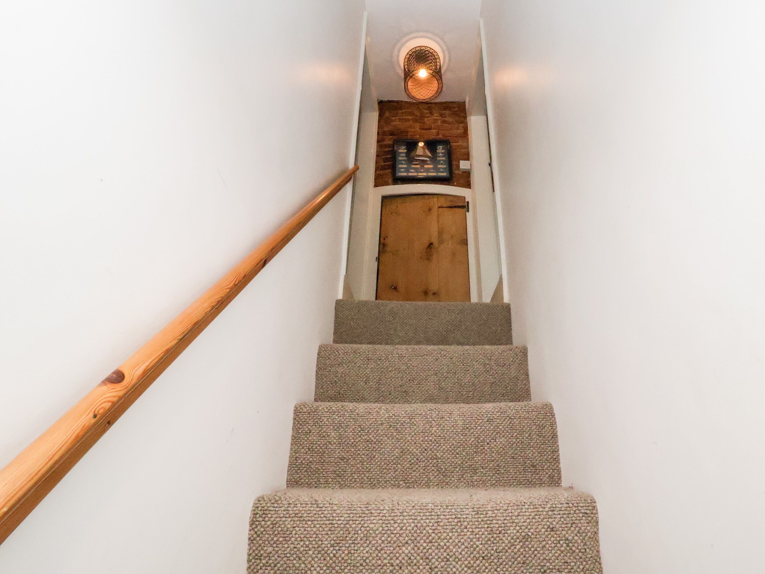 A staircase with wooden handrails and carpeted steps leading to a door with a brick wall and a light fixture above.