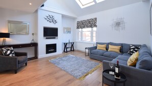 Ein modernes Wohnzimmer mit einem grauen Sofa, einem Couchtisch mit einer Weinflasche und einem Kamin.