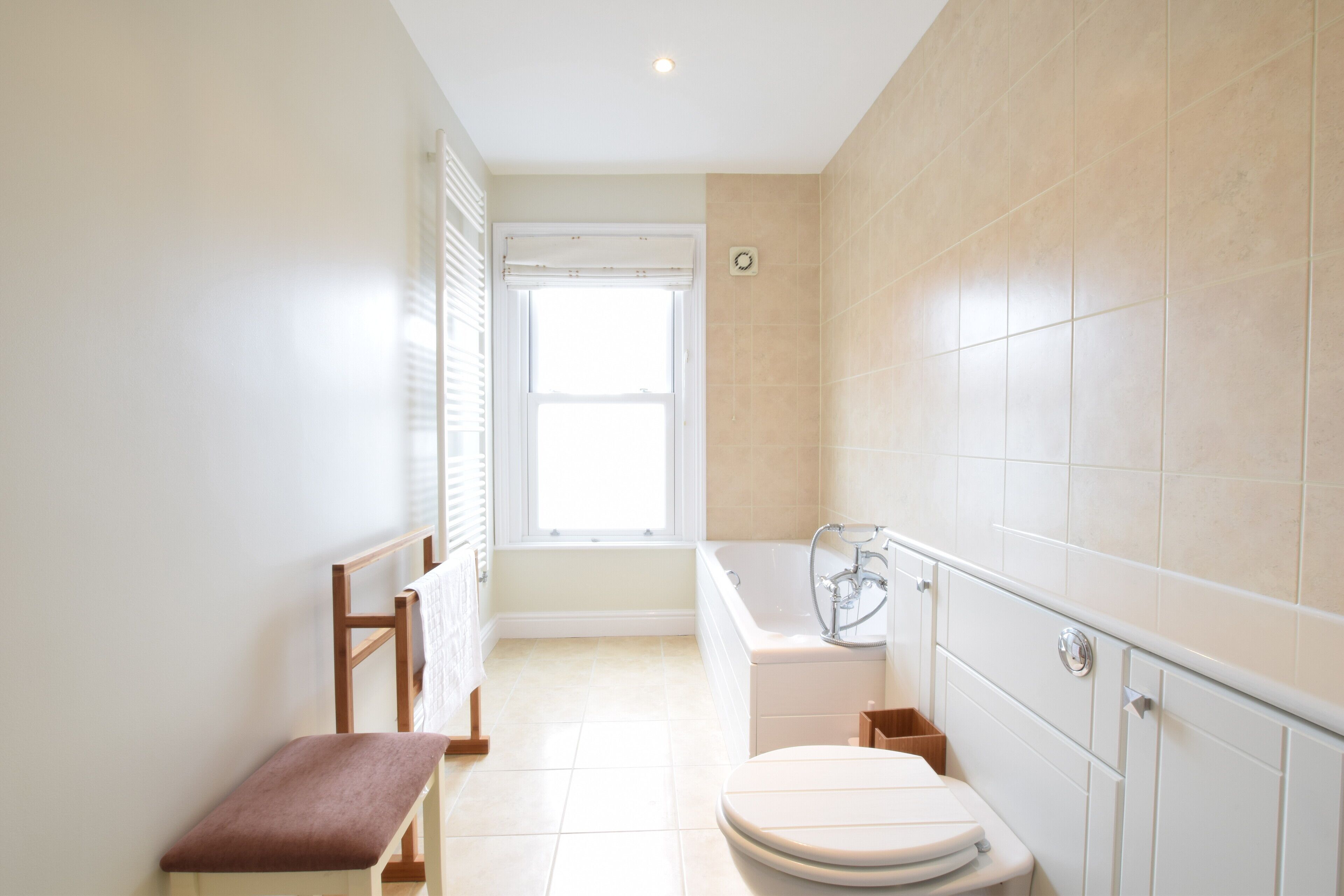 A bathroom with a bathtub, toilet, bench, and a window.