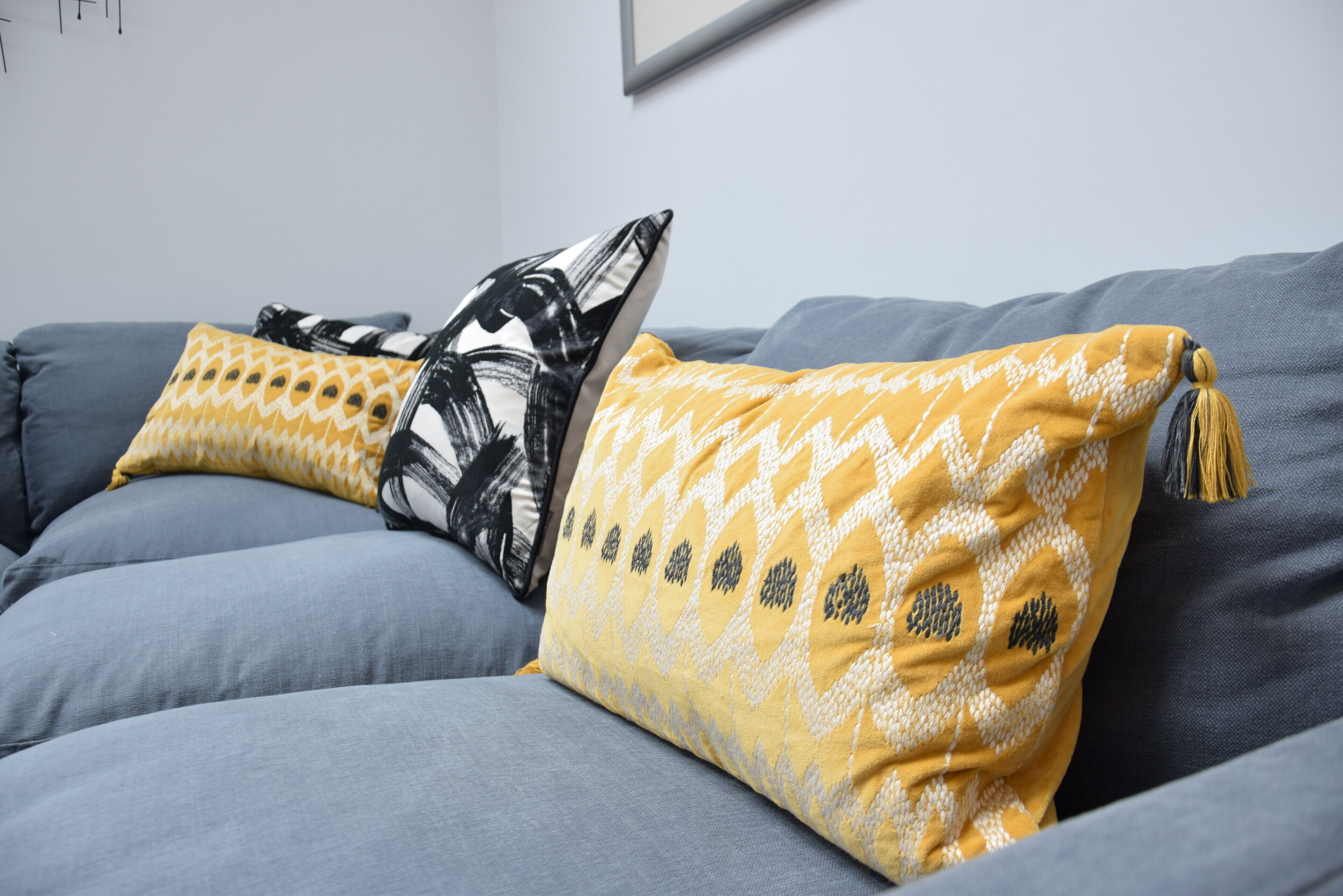 Um sofá cinzento com duas almofadas decorativas, uma com padrão abstrato preto e branco e outra com design geométrico amarelo e branco.