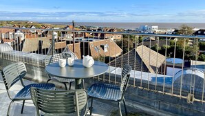 Eine Terrasse mit Tisch und Stühlen mit Blick auf eine Küstenstadt, Häuser und Meer.
