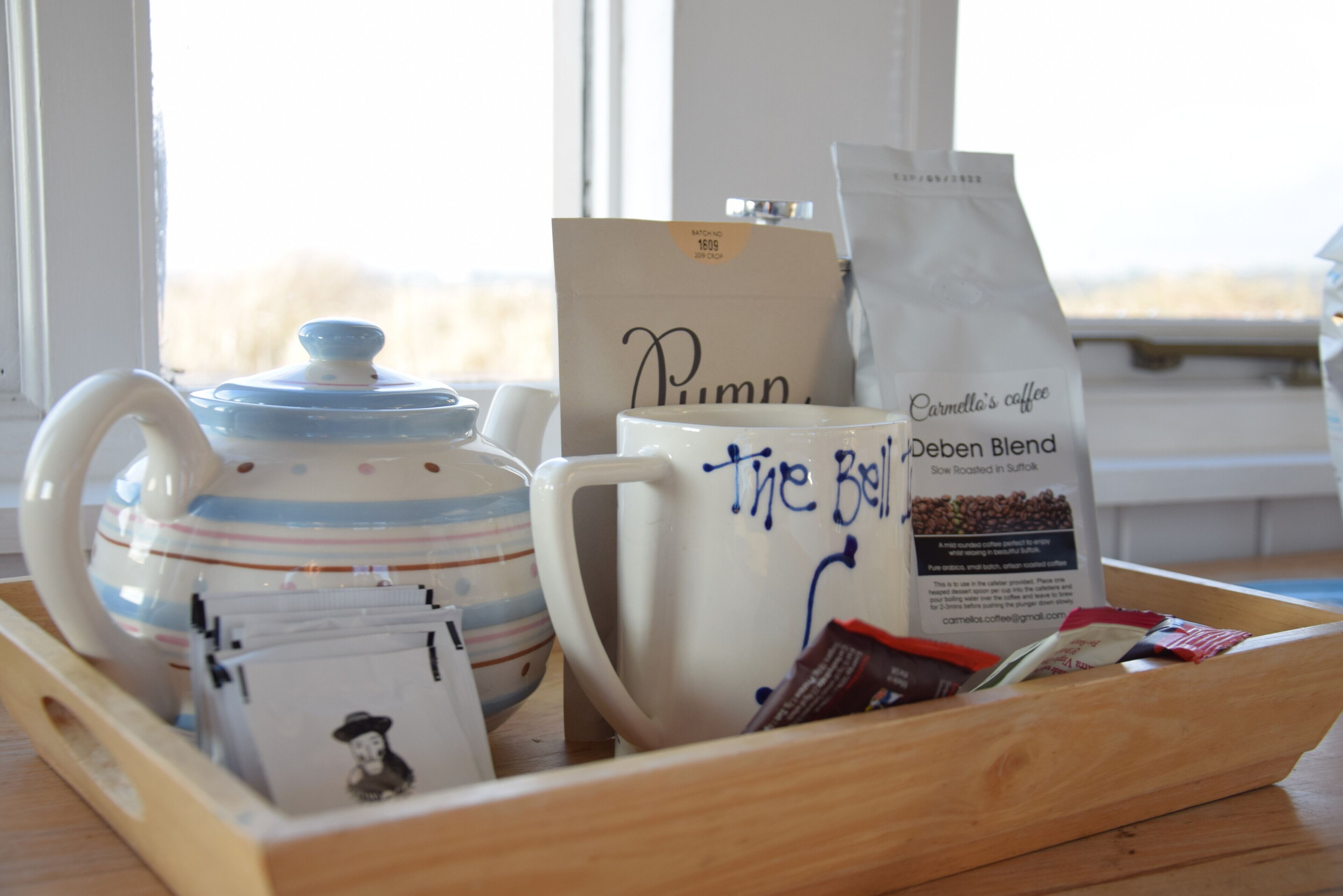 A tray with a teapot, mug, coffee packets, and a bag of coffee labeled 'Carmella's Coffee'.
