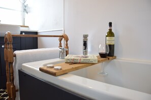 Un baño con un toallero de madera, un lavamanos blanco, una botella de vino y un vaso sobre una repisa de madera.