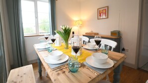 Ein Esstisch ist gedeckt mit weißen Tellern, Schüsseln und Gläsern, dazu ein Blumenstrauß in einer Vase und eine Lampe.