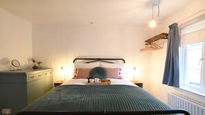 Ein Schlafzimmer mit Bett, Nachttischen, einem Schminktisch, einem Fenster mit Vorhängen und einer Pendelleuchte.
