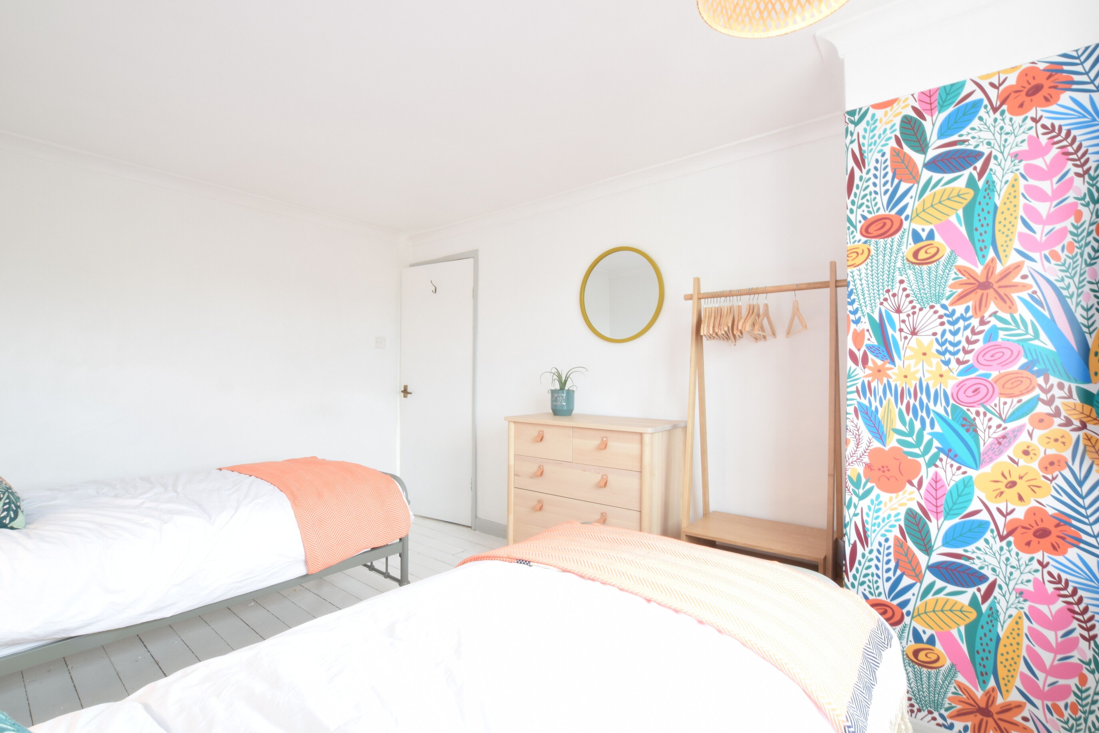 A bedroom with two beds, a dresser, a mirror, and a colorful floral curtain.
