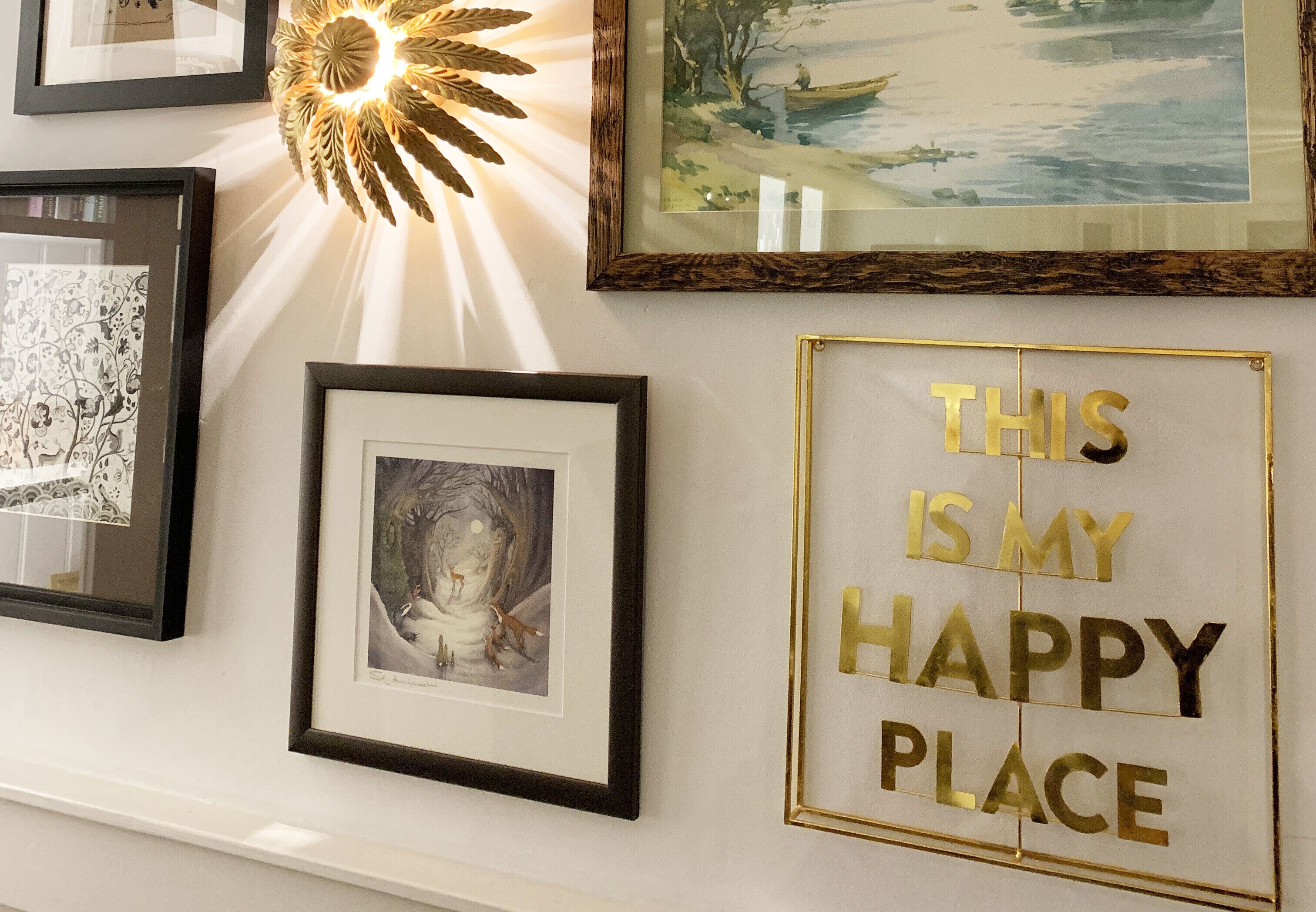 A wall with framed artwork, including a landscape painting, a black and white abstract piece, and a framed photograph. A decorative light fixture is also visible.